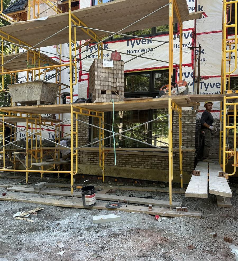 Mason building a brick chimney chase on scaffolding during a custom build