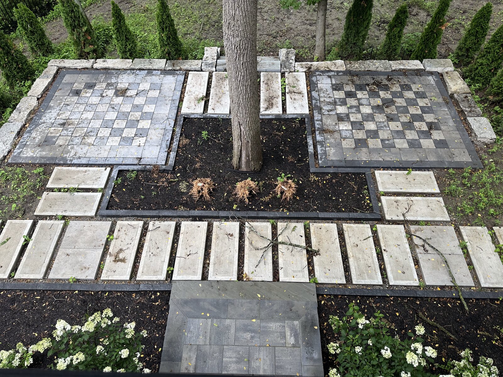 Custom paver walkway with inlaid stone checkerboard pattern around a mature tree