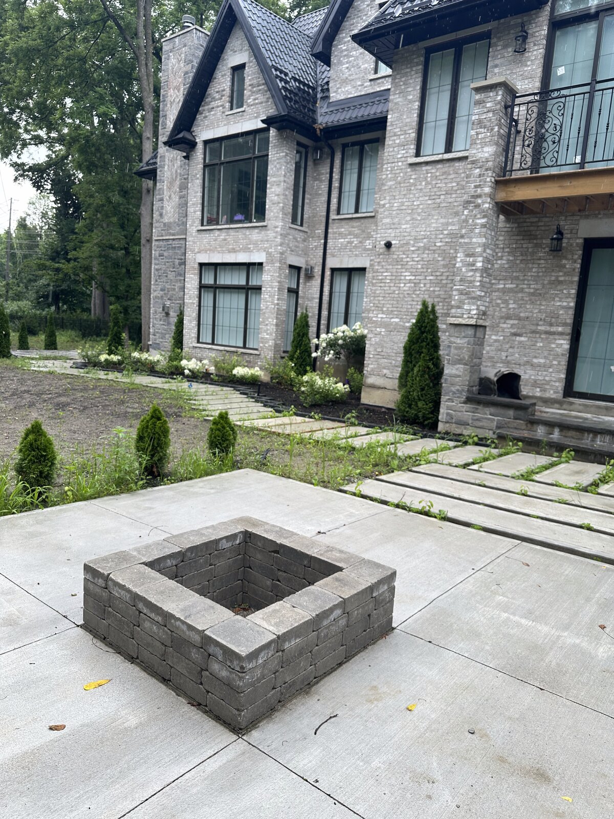 Paver patio with a built-in square fire pit surrounded by planting beds