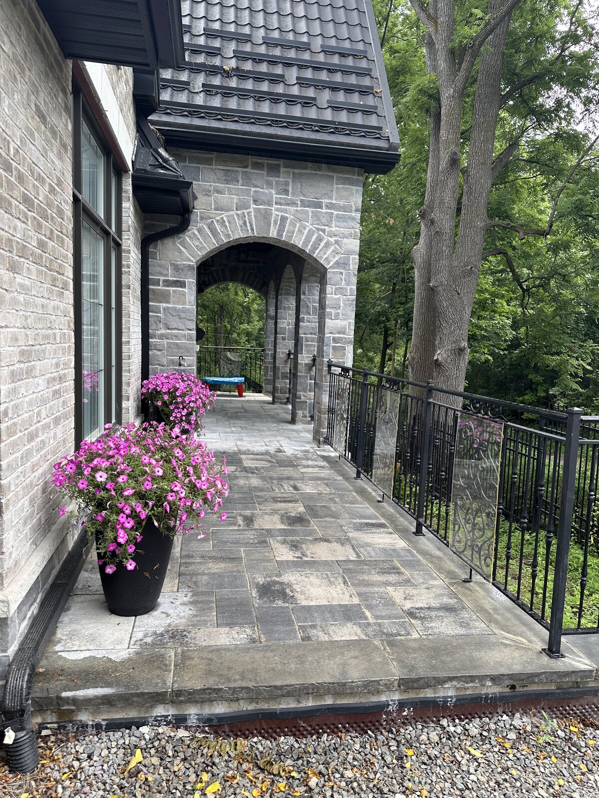 Covered stone walkway with container flower plantings alongside a custom home