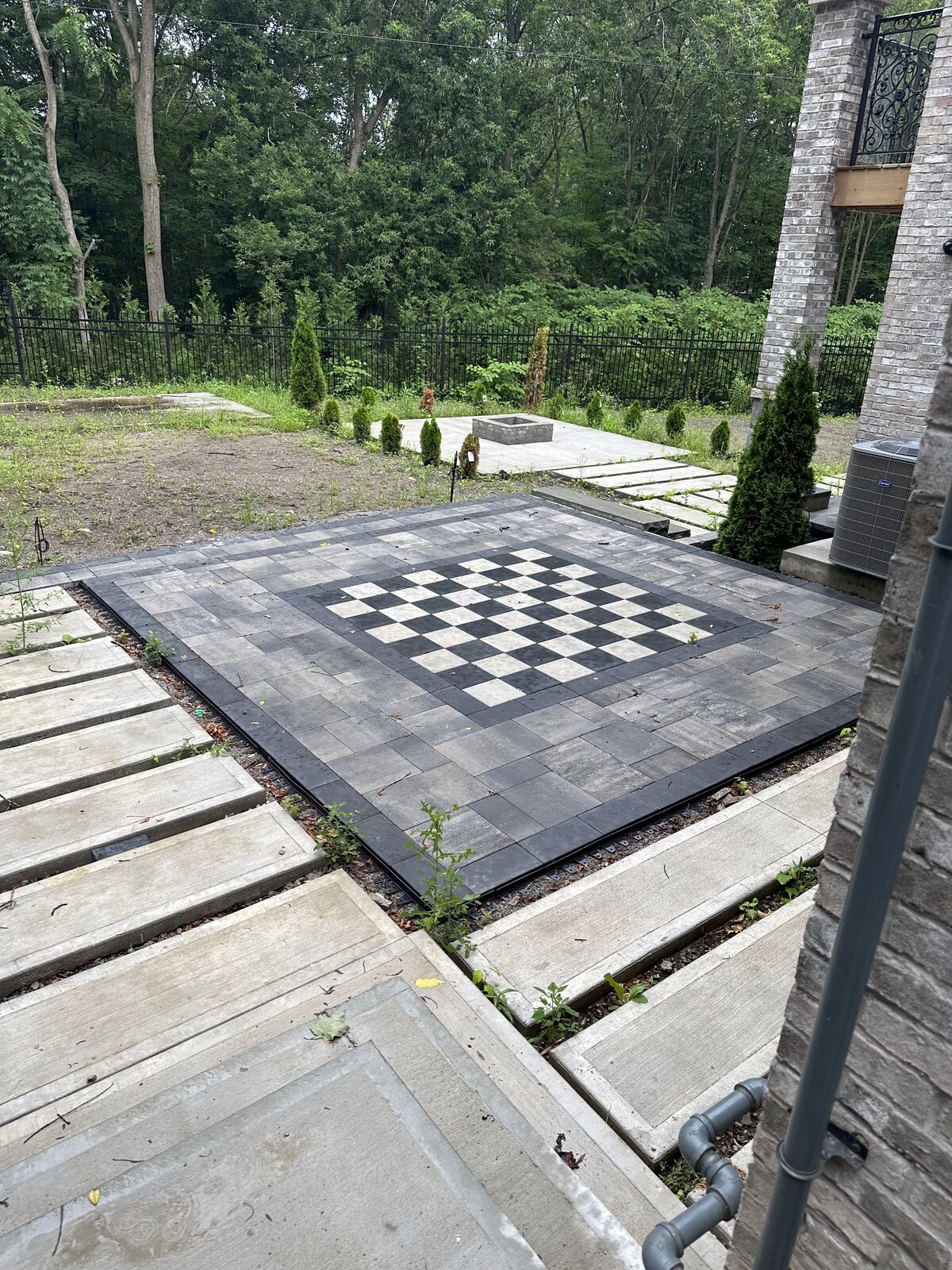 Custom paver patio with inlaid stone checkerboard pattern and built-in fire pit